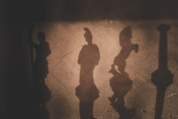 Shadows of Roman soldier statues on a wall, creating a dramatic and classical mood