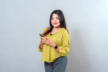Portrait of young Asian woman holding smartphone while smiling confidently at camera. Her friendly and fresh expression conveys trust, positivity, and modern digital lifestyle.