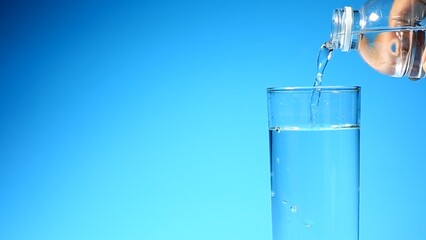 Pouring Water into a Glass: Crystal-clear water flows from a bottle into a glass, creating a...