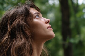 Naklejka premium Woman gazes upwards, possibly at trees. Her expression is pensive and serene, with a sense of wonder and connection to nature.