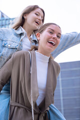 Two happy Caucasian young women enjoying a piggyback ride outdoors, laughing and having fun....