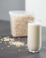 A glass of oat milk and oatmeal in a box on grey kitchen table. Vegan and non-dairy alternative milk
