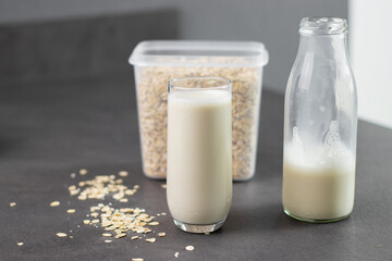 A glass of oat milk and oatmeal in a box on grey kitchen table. Vegan and non-dairy alternative milk