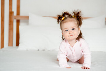 Fototapeta premium Funny baby girl in pink bodysuit on the bed in the bedroom smiling or laughing, cute little baby at home, place for text