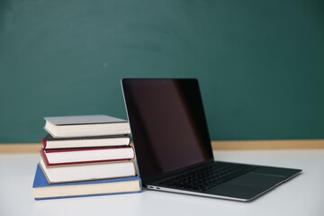 Stack of books and laptop on desk against chalkboard