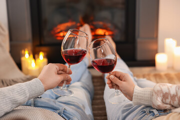 Couple with glasses of wine near fireplace on floor at home, selective focus