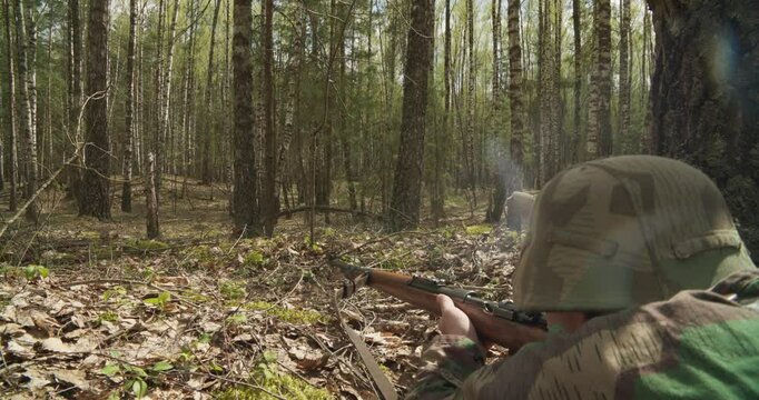 Reenactor Dressed As German Infantry Soldier Shoots From Rifle Carabine Mauser 98k In Ambush. War Ambush In Forest. Wermacht Military Uniform. Reenactment Tactic Game. Reload And Shooting From Rifle