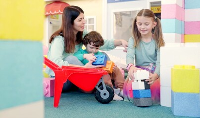 Happy young mother and two children in game center while playing with colorful foam plastic blocks...