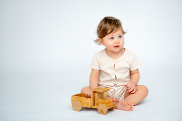 A baby boy is playing with a wooden typewriter on a white isolated background with a place for text in white knitted clothes. A small happy child rejoices and laughs, space for text