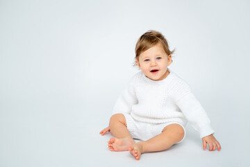 A baby boy on a white isolated background with a place for text is sitting in white knitted clothes. A small happy child in a winter sweater , space for text