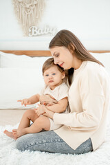 mom and baby on the bed at home hugging and kissing, mother and child playing and having fun, happy...