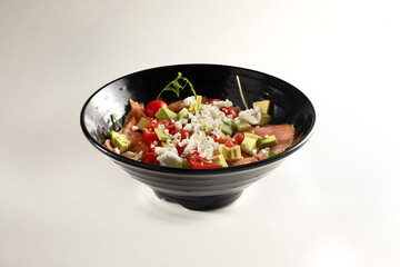 salad dressed with mozzarella, avocado, tomatoes and salmon. Black dish on white background