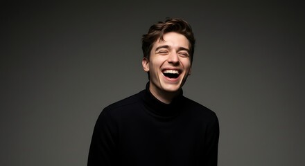 Obraz premium Happy Young Man Laughing Against a Gray Background