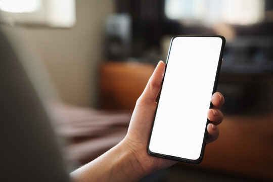 Young woman hold smartphone with white screen while sitting on a couch - Powered by Adobe