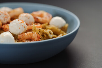 Penne pasta with shrimps and mozzarella and pesto in blue bowl with copy space