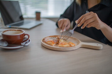 An Asian female student is sitting at a table in her office eating pizza.