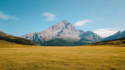 Fototapeta premium Majestic mountain peaks rise above vast green meadow under clear blue sky