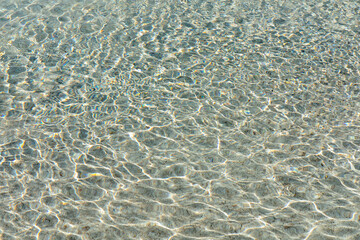 A close-up view of clear pool water, with gentle ripples and soft reflections, creating a peaceful atmosphere. The sunlight dances on the surface, highlighting the tranquil beauty of the water