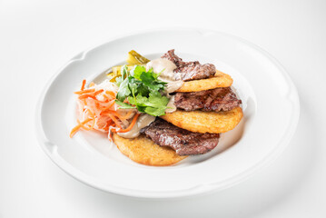 A plate features grilled slices of beef served with crispy plantains and a side of fresh salad. The dish is garnished with cilantro and creamy dressing, highlighting vibrant flavors.