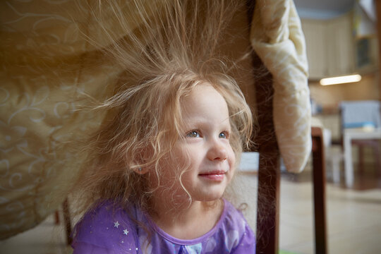 A child at home plays in a house built from a blanket.