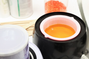 Hot depilatory wax in heater and other products on table, closeup