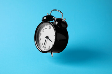 Black alarm clock in air on light blue background