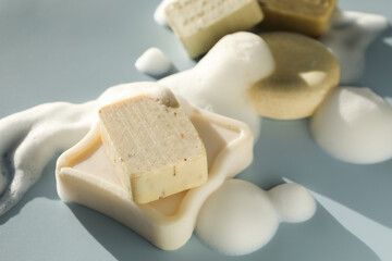 Soap bars with foam on grayish blue background, closeup