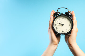 Woman with black alarm clock on light blue background, closeup. Space for text