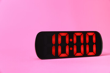 Digital alarm clock showing 10:00 o'clock on pink background, space for text