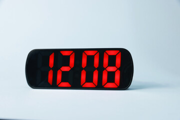 Digital alarm clock showing 12:08 o'clock on grey background