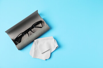 Naklejka premium Case with stylish glasses and cleaning cloth on light blue background, top view. Space for text