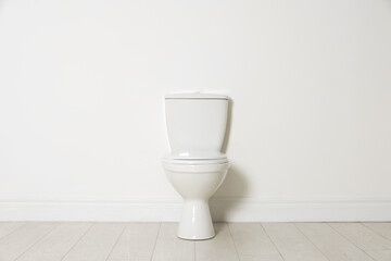 Ceramic toilet bowl near white wall indoors