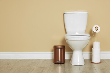 Toilet bowl, trash bin and paper rolls near beige wall indoors. Space for text
