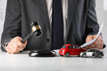 Auto accident law. Man with document striking gavel at table indoors, closeup