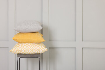 Soft decorative pillows on stool near grey wall. Space for text