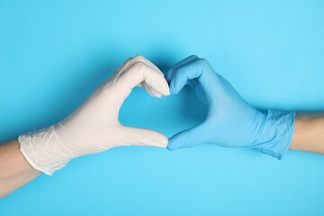 Doctors in medical gloves making heart gesture on light blue background, closeup