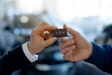 Closeup image of car keys being handed from salesman to customer at modern car dealership center, unrecognizable man buying new automobile, enjoying purchase, cropped shot