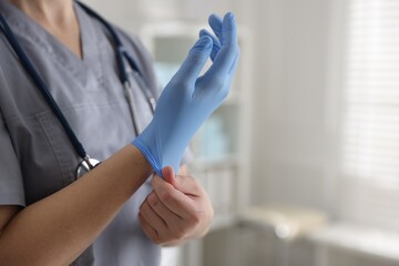 Medical worker putting on gloves in hospital, closeup. Space for text