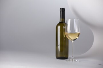Bottle and glass of tasty wine on light grey background. Space for text