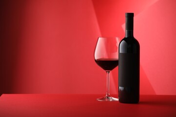Bottle and glass of tasty wine on red background. Space for text