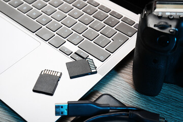 USB cable, SD memory cards, camera and laptop on wooden table, closeup