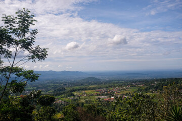 A wide panoramic view of a lush valley dotted with small houses and rice fields under a blue sky...