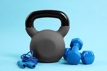 Kettlebell, jumping rope and dumbbells on light blue background