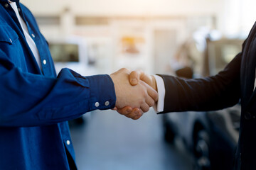 Closeup of handshake between customer and salesman in car dealership center, manager greeting man with buying new vehicle, selective focus on hands with blurred showroom background
