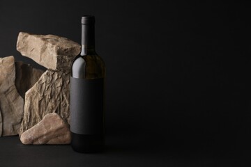 Naklejka premium Bottle of wine and rocks on black background, space for text