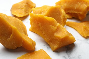 Pieces of natural beeswax for making candles on white marble table, closeup