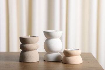 Stylish candlesticks with burning candles on wooden table indoors