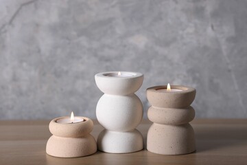 Stylish candlesticks with burning candles on wooden table near grey marble wall indoors