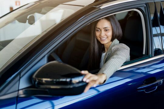 Millennial woman adjusting car side mirror while sitting inside new car in dealership showroom, happy young female enjoying driving, celebrating purchase new vehicle, closeup