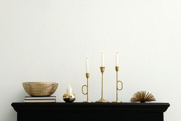Stylish candlesticks with burning candles and other decor on fireplace near white wall indoors